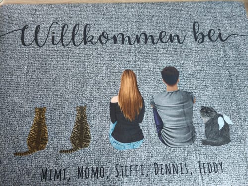Kundenfoto einer personalisierten grauen Fußmatte, die ein Paar und drei Katzen von hinten zeigt, eine davon mit Engelsflügeln.