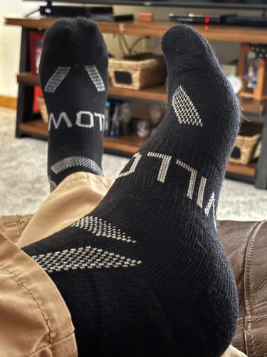 Reviewer lounging in a recliner with their feet up, wearing the black Men's Alpaca Socks.