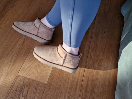 Een klant draagt de UGG Classic Ultra Mini Boot Chestnut op een houten vloer.