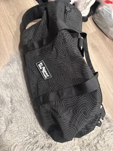 Reviewer's black Cash Duffle Bag with a white topographic 'Pathway' pattern, shown on a grey rug.