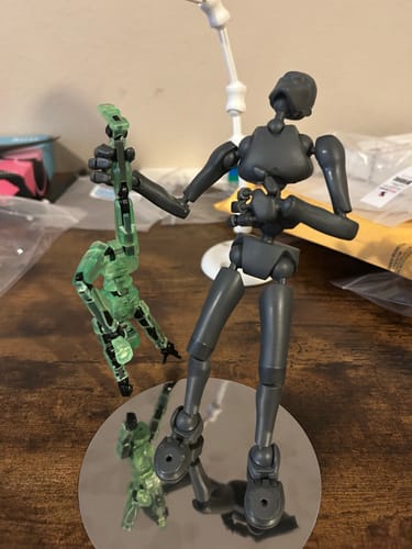 Customer's grey Stickybones figure on its base, holding a smaller figure, supported by the white Fly-Rig.