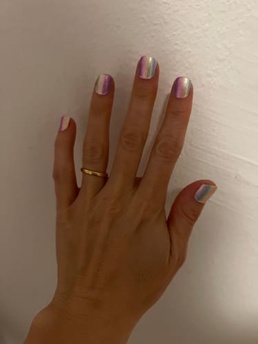 Hand einer Kundin, die die schimmernden Rainbow Shimmer Nagelfolien vor einer weißen Wand zeigt.
