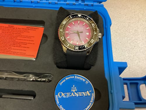 Reviewer's Oceaneva watch with a purple dial and black bezel, shown in its blue protective case.