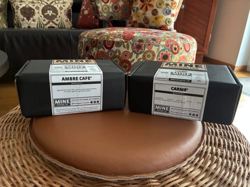 Cliente mostra le scatole nere dei profumi AMBRE CAFE' e Carme su uno sgabello.