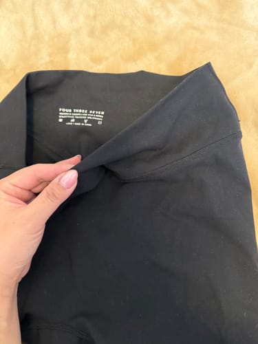 Close-up of a reviewer holding the waistband of the black Essentials Legging, showing the inner tag.