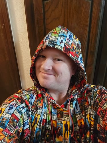 Reviewer smiling while wearing the Marvel "Corner Box Brigade" Performance Hoodie with the hood up, showing the colorful pattern.