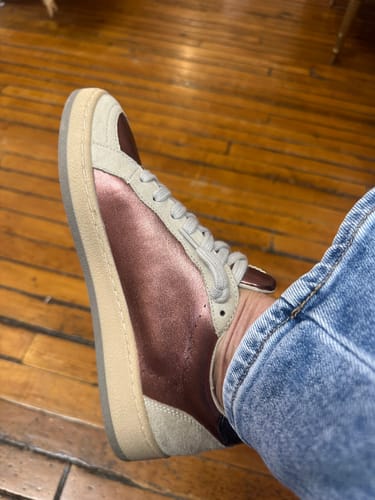 A side view of a reviewer's stylish sneaker, showing the metallic fabric and suede details.