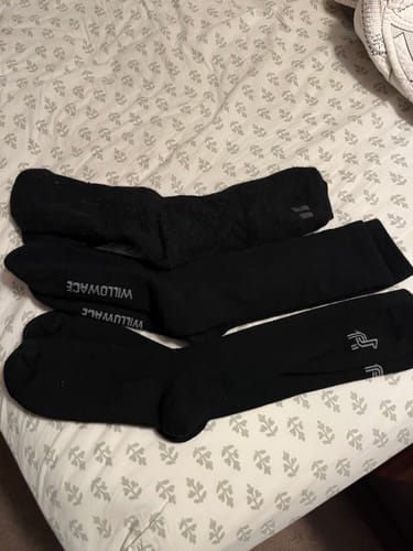 Reviewer's three pairs of black alpaca boot socks from different brands laid out on a bed for comparison.