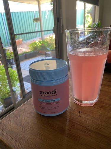 Customer's tub of Pink Lemonade sits on a wooden counter next to a glass of the prepared pink drink.