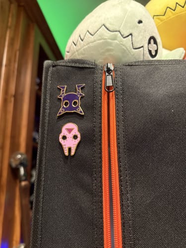 Reviewer's purple and pink Scavenger Mask pins attached to a black bag with an orange zipper.