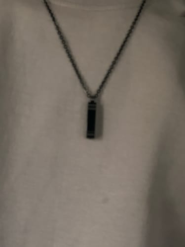 Close-up of a customer wearing the Rectangle Bar Urn Pendant on a chain against a white shirt.