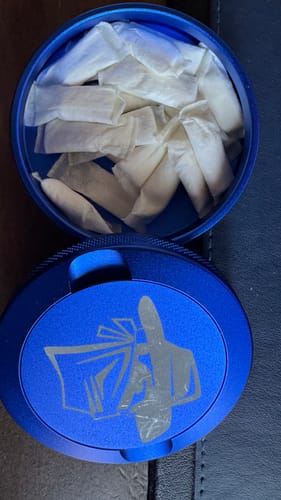Customer's open blue circular tin filled with Mountain Wintergreen Nicotine Pouches, with the lid resting in front.