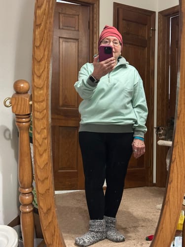 Reviewer taking a mirror selfie while wearing black leggings, a mint green sweatshirt, and a red beanie.