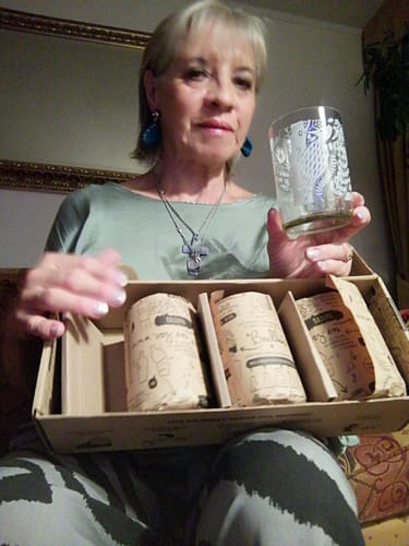 Reseñadora mostrando un vaso ilustrado del juego Aves de Chile, con la caja abierta en su regazo.