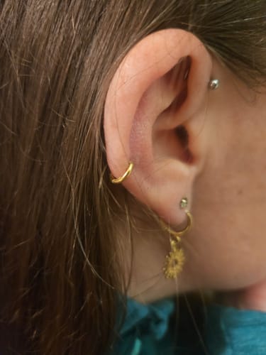 Customer's ear wearing the Simple Clicker Gold earring in a snug cartilage piercing, with other earrings visible.