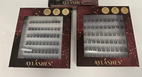 Ein Kunde zeigt zwei Schachteln des AYLASHES Bundle Builders auf einem weißen Tisch.