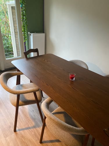 Recensent toont de walnootkleurige Brinn eettafel met afgeronde hoeken in een eetkamer.