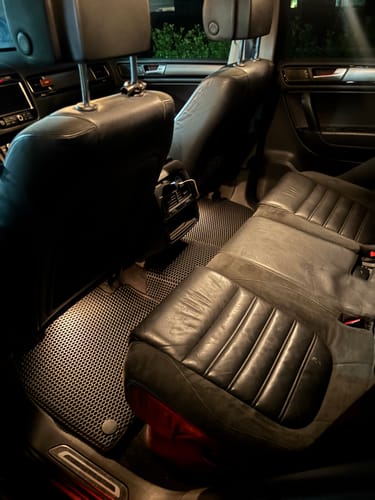 Recenzent pokazuje idealnie dopasowane czarne dywaniki samochodowe w tylnej części swojego auta.