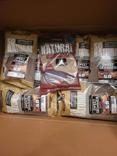 Klant toont een doos vol met diverse SO NATURAL GROUNDBAIT zakken, waaronder de Sweet Skimmer en Natural varianten.