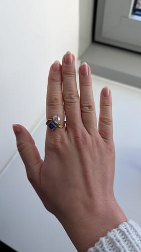 Customer's hand showing the Navae Birthstone Ring with a blue radiant-cut and a clear pear-cut stone.