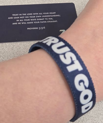 Reviewer's close-up of the blue Trust God Bible Verse Bracelet on their wrist with its scripture card in the background.