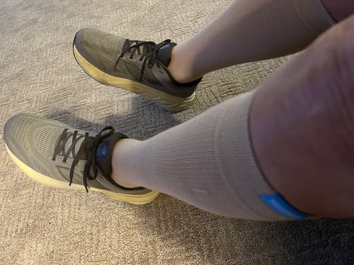 Reviewer sitting on a carpet wearing light-colored Performance Eucalyptus Compression Socks and running shoes.