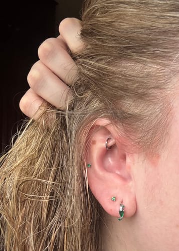 Customer wearing the silver and green Ethereal huggies in a close-up view of their ear.