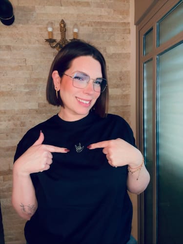 לקוחה לובשת חולצת טי שירט LOUDER by Émily שחורה ומצביעה על הרקמה.