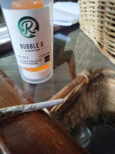 Customer's Bubble G packaging with a rolled cigarette on a glass table.