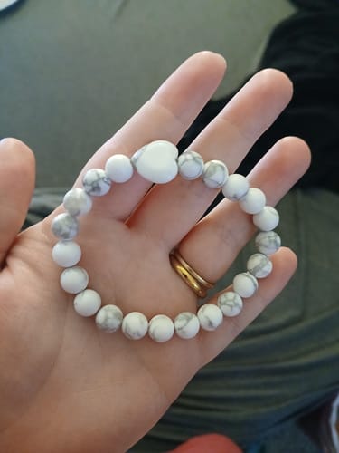 Reviewer holding a crystal bracelet with white and grey marbled beads and a central white heart bead.