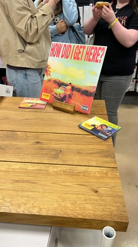 Reviewer at the Louis Tomlinson Listening Event with merchandise displayed on a wooden table.