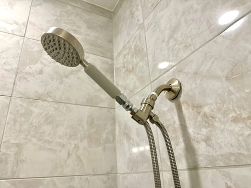 Customer's Universal Shower Head Holder installed in a tiled shower, holding a handheld shower head.
