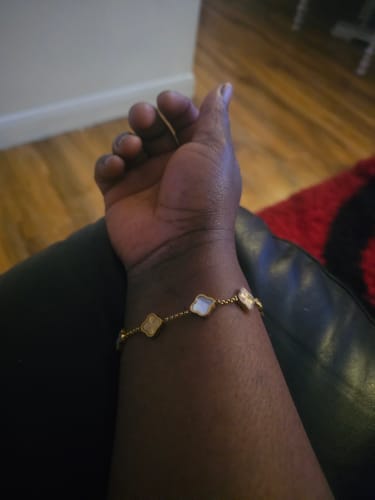 Customer's wrist wearing a gold-colored bracelet with white and gold clover-shaped charms.