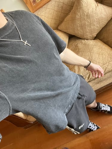 Cliente mostrando el colgante de crucifijo plateado sobre una camiseta gris oscuro.
