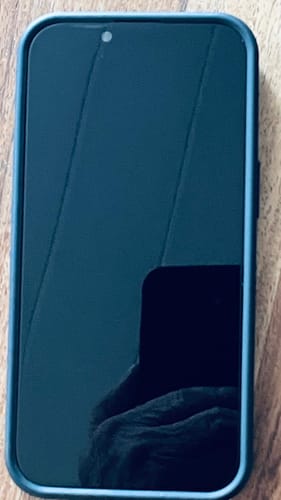 Rezensent zeigt die 3-in-1-Schutzfolie, die auf einem iPhone mit dunklem Bildschirm angebracht ist.