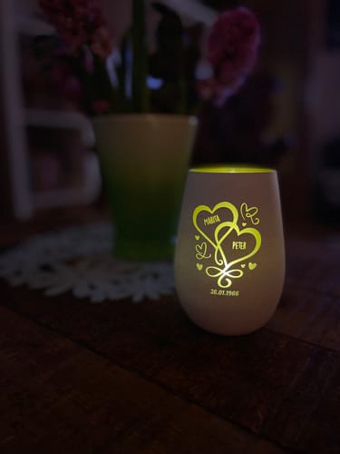 Kunde zeigt das personalisierte LED-Teelicht in einem gravierten Glas, das auf einem Holztisch warm leuchtet.