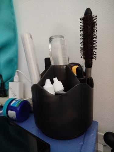 Cliente usando el organizador de escritorio en su buró para guardar un cepillo, frascos y un control remoto.