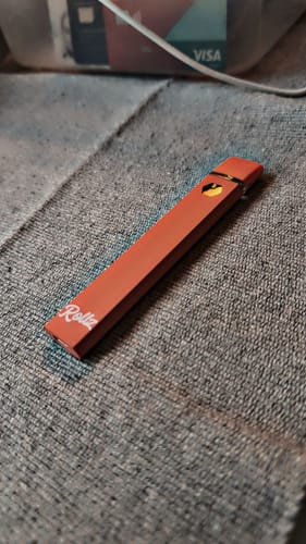 Customer's terracotta-colored ROLLZ THCA Vape pen resting on a grey textured cloth.