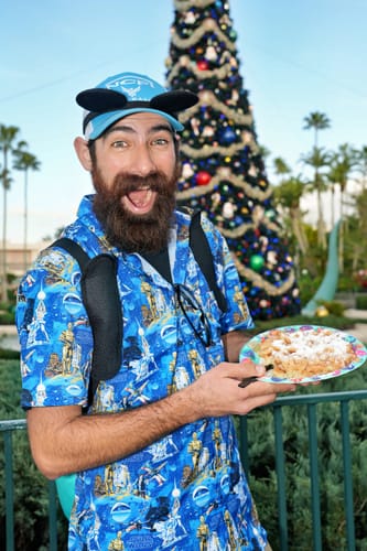 Reviewer smiling in the blue Star Wars "Luke Sleepwalker" shirt while at a theme park with a Christmas tree.