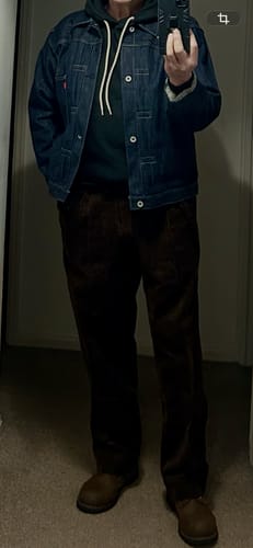 Reviewer in a mirror selfie showing the full-length fit of the brown corduroy trousers, paired with a denim jacket.