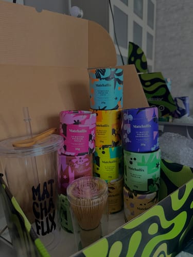 Cliente mostrando varios botes de Té Matcha Premium y accesorios en una caja de envío abierta.