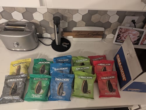 Customer's variety of Smackin' sunflower seed bags, including Cracked Pepper, arranged on a kitchen counter.