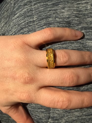 A customer's hand wearing the gold Aureum ring, showing the textured gold foil inlay against a grey fabric.