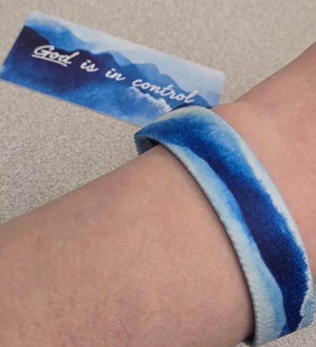 Reviewer wearing the blue and white God Is In Control Bracelet on their wrist, with the matching card in the background.