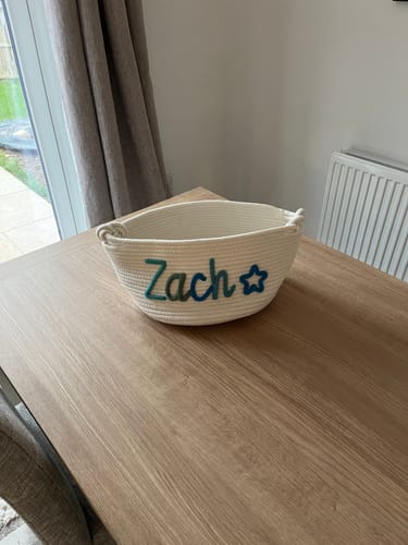 Customer's personalized woven basket with 'Zach' and a star in blue, sitting on a wooden table.