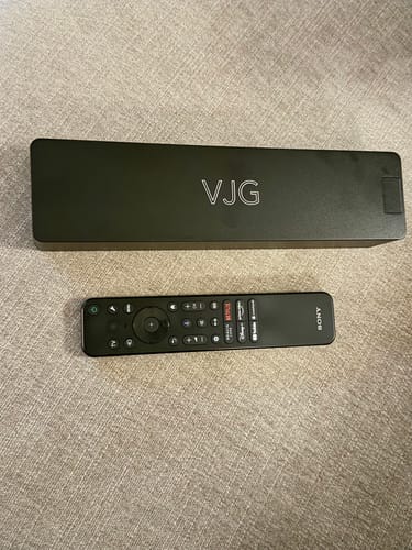 Customer's dark Weekly Case shown closed next to a TV remote for size comparison on a textured surface.