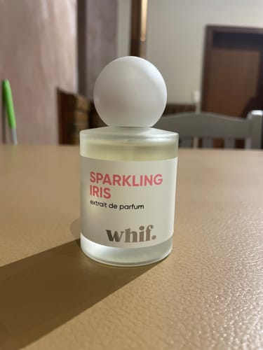 Customer's bottle of Sparkling Iris perfume on a table. The frosted bottle has a round, white cap.