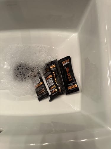 Reviewer washing several packets of SuperCharged Honey in a soapy white sink.