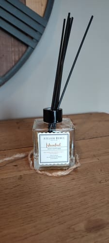 Recensent toont de vierkante fles Istanbul Geurstokjes met zwarte stokjes op een houten tafel.