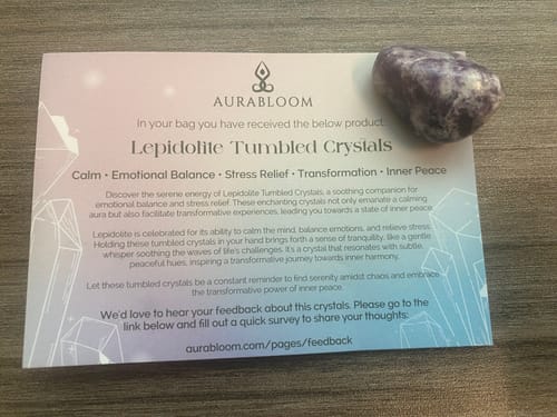 Reviewer's purple tumbled crystal from their monthly subscription, shown next to its descriptive card on a table.